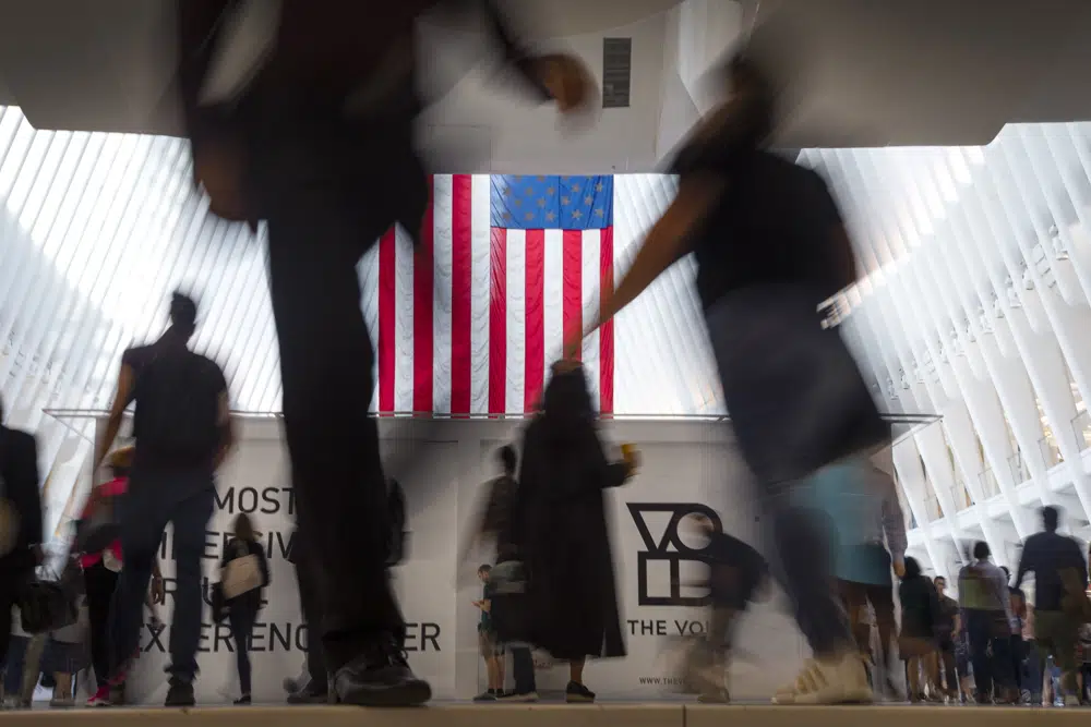 FILE - People walk past an American flag inside the Oculus, part of the World Trade Center transportation hub, at the start of a work day in New York, Sept. 11, 2019. American lore is full of tales of a nation built on the foundations of individualism. In reality, loneliness in America can be deadly. In May 2023, the U.S. surgeon general declared it an epidemic, saying that it takes as deadly a toll as smoking. (AP Photo/Wong Maye-E, File)